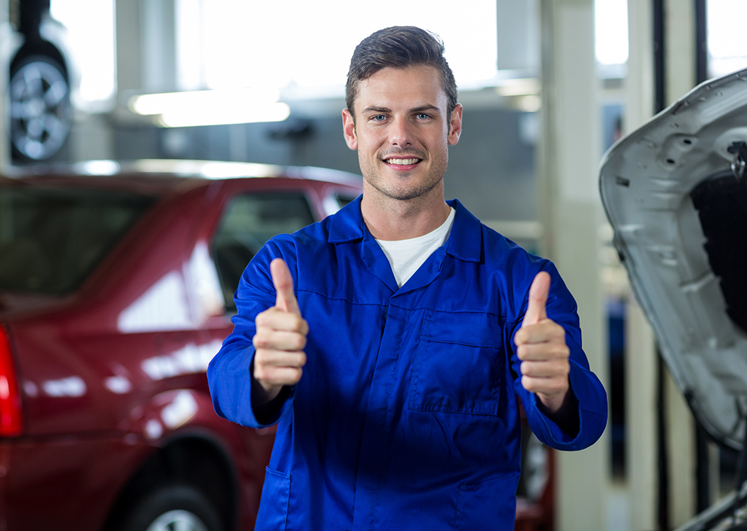 Portrait of smiling mechanic standing in repair shop showing thumbs up